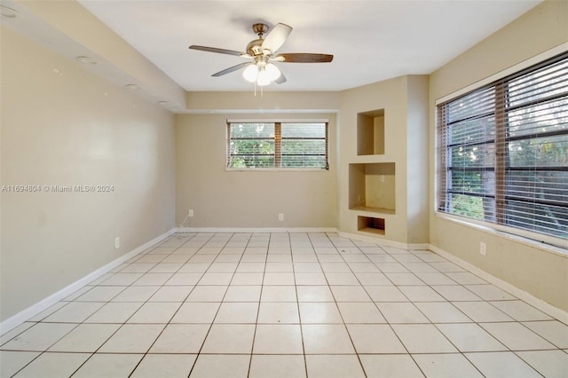 empty room featuring built in shelves, ceiling fan, and light tile patterned floors