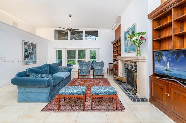 living room featuring a towering ceiling, ceiling fan, crown molding, light tile patterned floors, and a fireplace