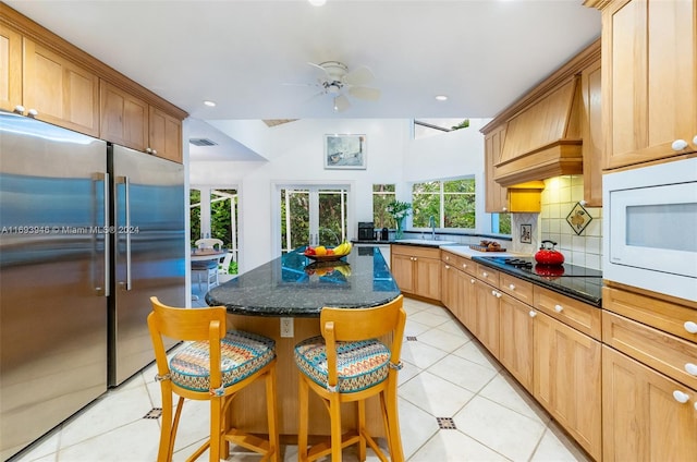 kitchen featuring a center island, premium range hood, white microwave, decorative backsplash, and high quality fridge