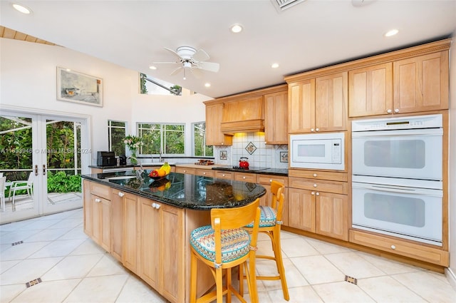 kitchen with white appliances, a center island, vaulted ceiling, and dark stone countertops