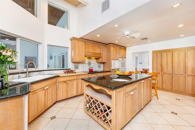 kitchen with sink, tasteful backsplash, dark stone counters, a center island with sink, and light tile patterned flooring