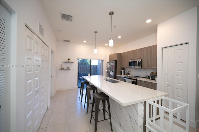 kitchen with a breakfast bar, sink, hanging light fixtures, an island with sink, and appliances with stainless steel finishes