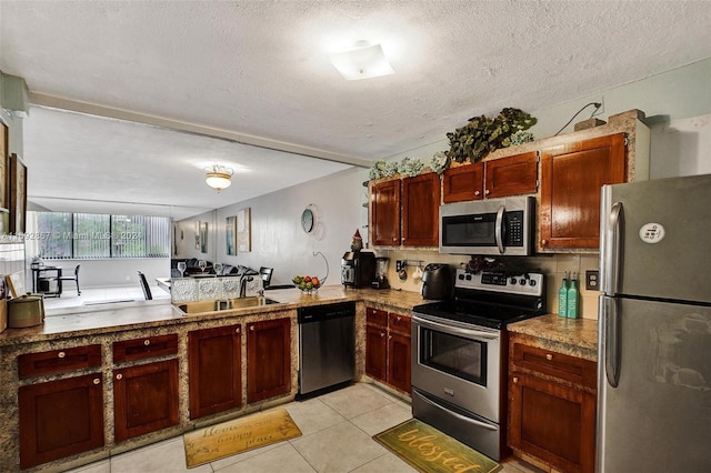 kitchen with sink, light tile patterned floors, a textured ceiling, appliances with stainless steel finishes, and kitchen peninsula