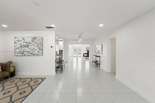 hallway featuring french doors, light tile patterned floors, and brick wall