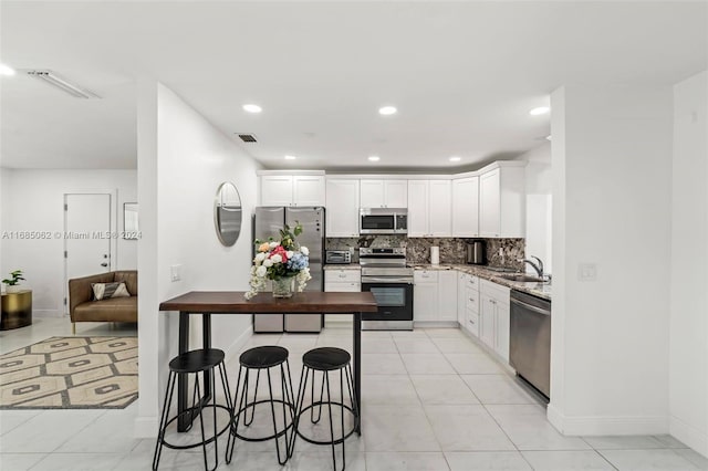 kitchen featuring decorative backsplash, light stone counters, a kitchen bar, white cabinetry, and stainless steel appliances