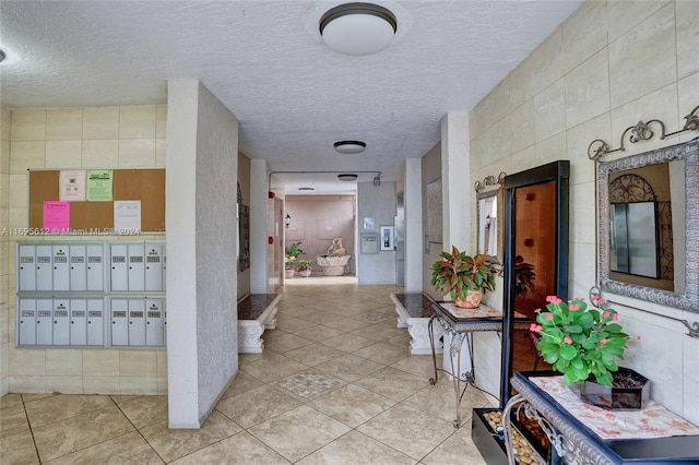 hall featuring a textured ceiling, light tile patterned flooring, and a mail area