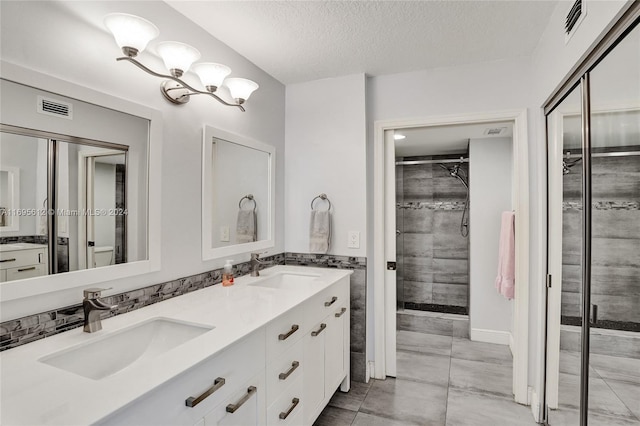 bathroom with vanity, a textured ceiling, tiled shower, and tile patterned flooring