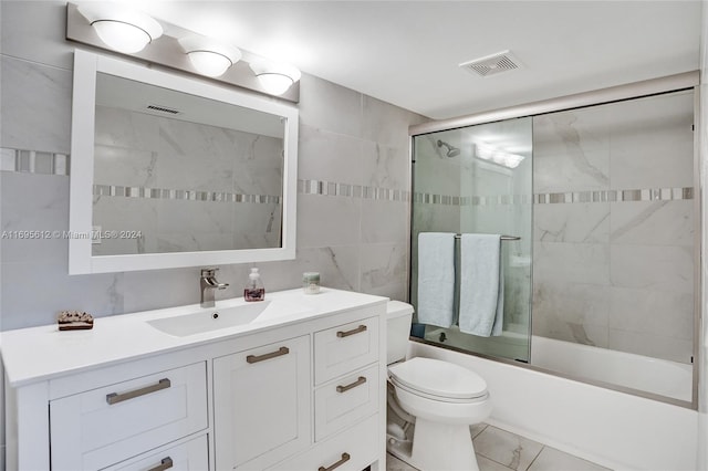 full bathroom featuring combined bath / shower with glass door, vanity, toilet, and tile walls