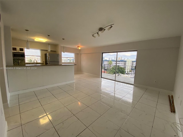 unfurnished living room with track lighting, plenty of natural light, and sink