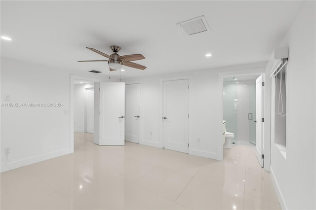 unfurnished bedroom featuring ceiling fan, light tile patterned floors, ensuite bathroom, and two closets