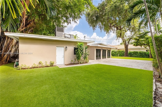 back of house featuring a garage, cooling unit, and a lawn