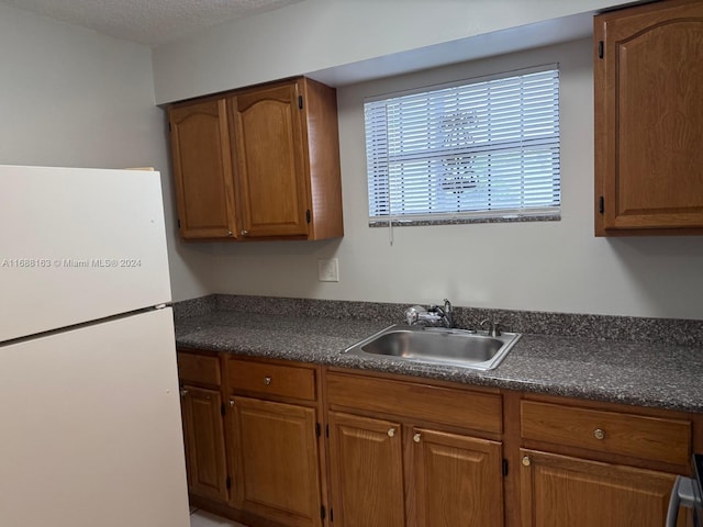 kitchen featuring a textured ceiling, white refrigerator, and sink