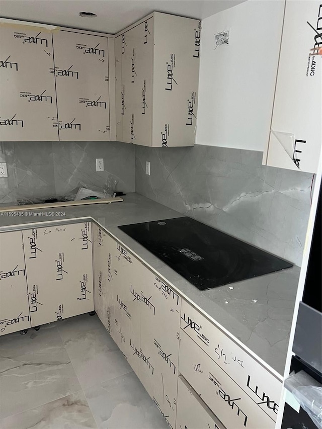 9801 Collins Ave Unit 15P-, Newly Renovated, Bal Harbour, FL 33154 - kitchen with backsplash, black electric stovetop, light marble finish floors, white cabinets, and light countertops