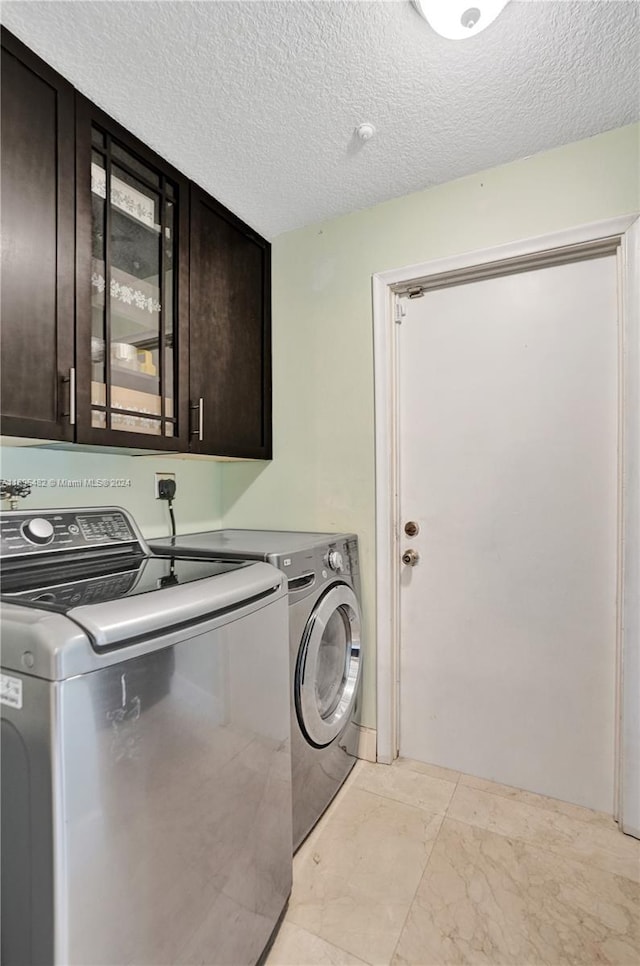 laundry room with cabinets, a textured ceiling, and washing machine and dryer