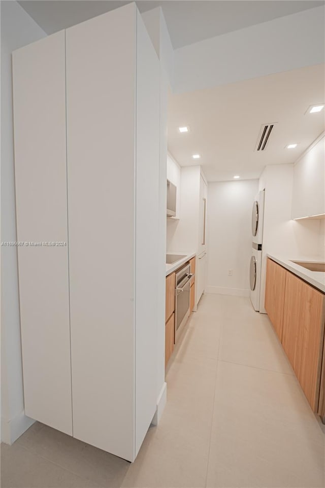 kitchen featuring light tile patterned floors, white cabinetry, stacked washer / drying machine, and stainless steel oven