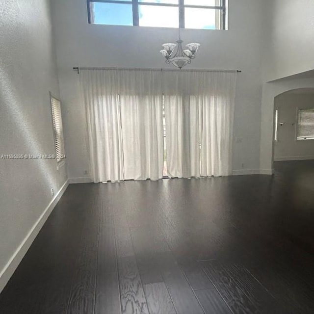 spare room featuring a notable chandelier, dark hardwood / wood-style flooring, and a towering ceiling