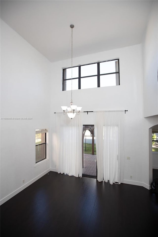 unfurnished living room featuring a high ceiling, dark hardwood / wood-style flooring, and an inviting chandelier