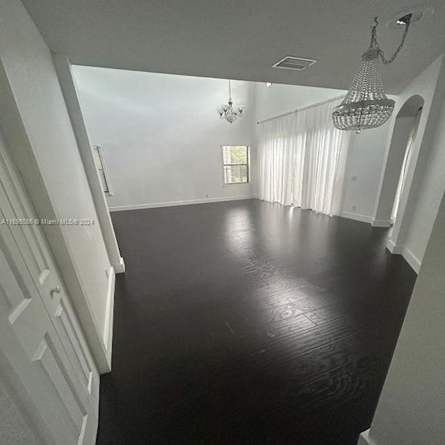 spare room with a chandelier and dark wood-type flooring