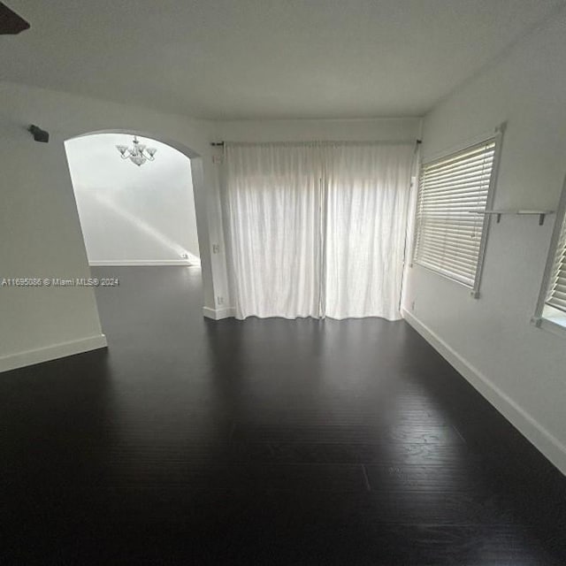 spare room with dark hardwood / wood-style floors and an inviting chandelier