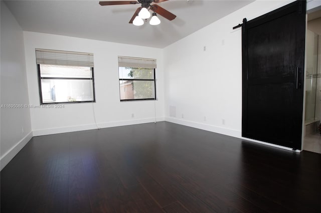 empty room featuring a barn door, ceiling fan, and dark wood-type flooring