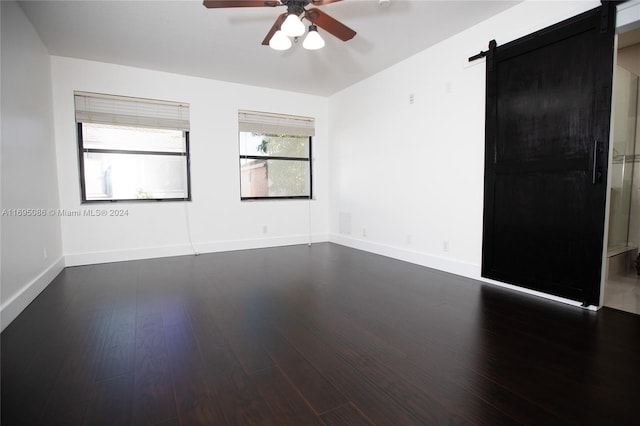 empty room featuring a barn door, dark hardwood / wood-style floors, and ceiling fan