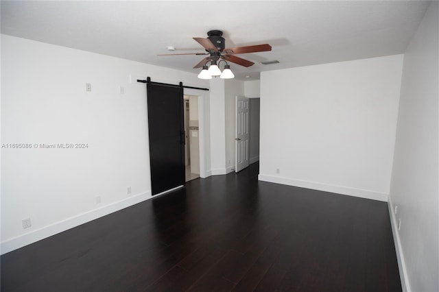 unfurnished room with ceiling fan, a barn door, and dark hardwood / wood-style flooring