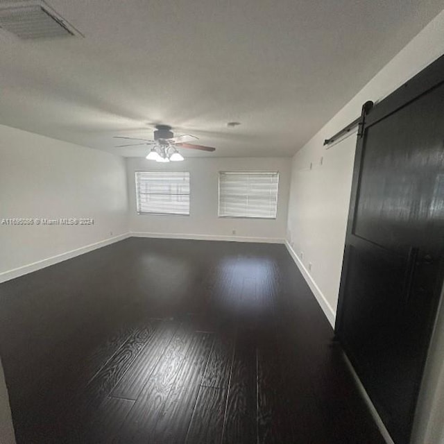 empty room featuring a barn door, ceiling fan, and dark wood-type flooring