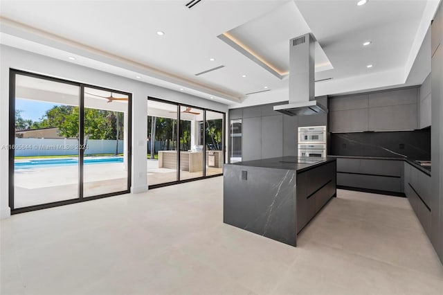 kitchen featuring a raised ceiling, double oven, extractor fan, ceiling fan, and a spacious island