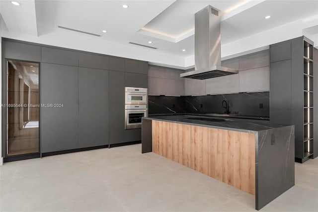 kitchen featuring island exhaust hood, backsplash, black electric cooktop, a raised ceiling, and double oven