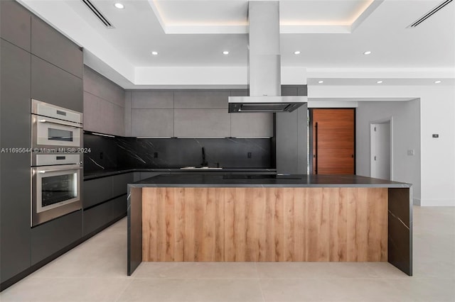 kitchen with decorative backsplash, a center island, island range hood, and a tray ceiling