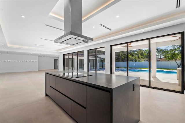 kitchen with ceiling fan, black electric cooktop, a tray ceiling, a large island, and island exhaust hood