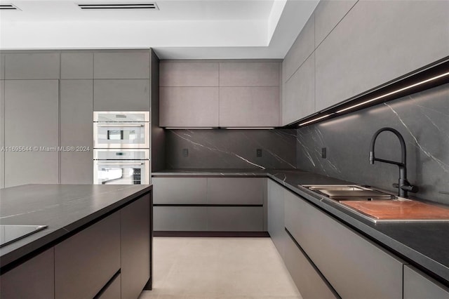 kitchen featuring stainless steel double oven, gray cabinets, tasteful backsplash, and sink