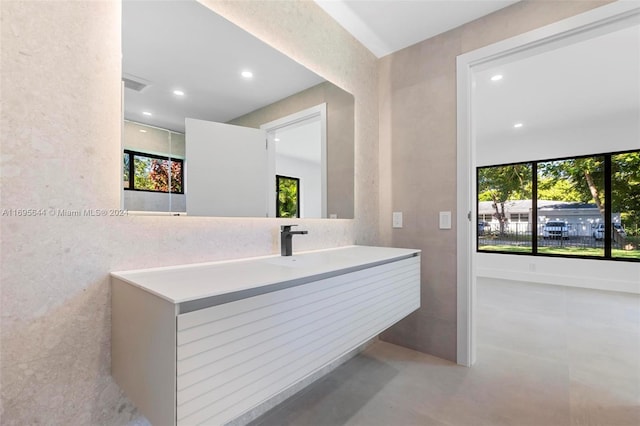 bathroom with concrete flooring, vanity, tile walls, and a healthy amount of sunlight