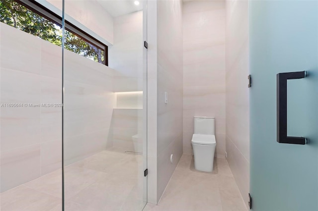 bathroom featuring tile patterned floors, toilet, and tile walls