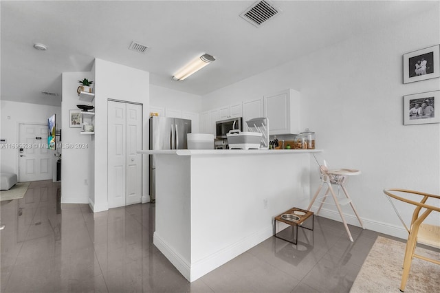 kitchen with white cabinetry, stainless steel appliances, a kitchen breakfast bar, tile patterned flooring, and kitchen peninsula