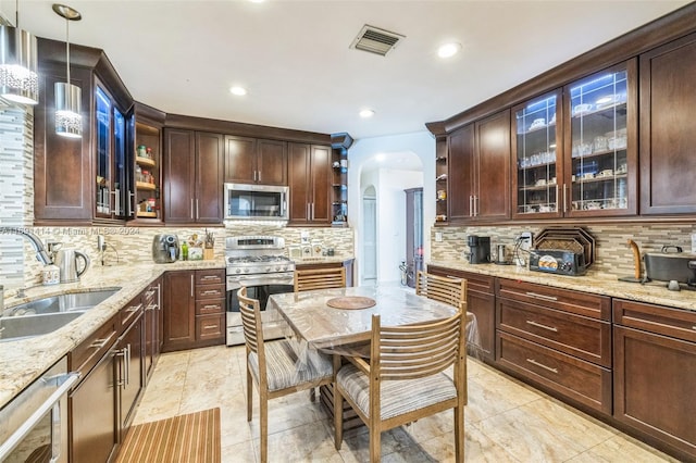 kitchen with backsplash, hanging light fixtures, sink, light stone countertops, and appliances with stainless steel finishes