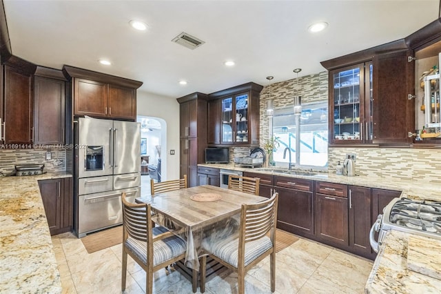 kitchen with pendant lighting, sink, appliances with stainless steel finishes, tasteful backsplash, and light stone counters