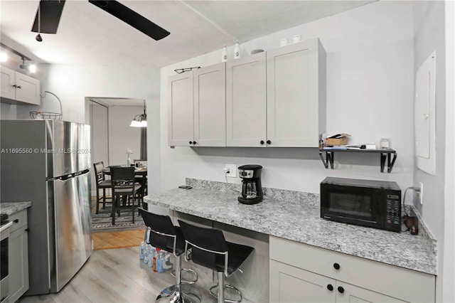 kitchen featuring stainless steel refrigerator, white cabinetry, ceiling fan, light stone countertops, and light hardwood / wood-style flooring