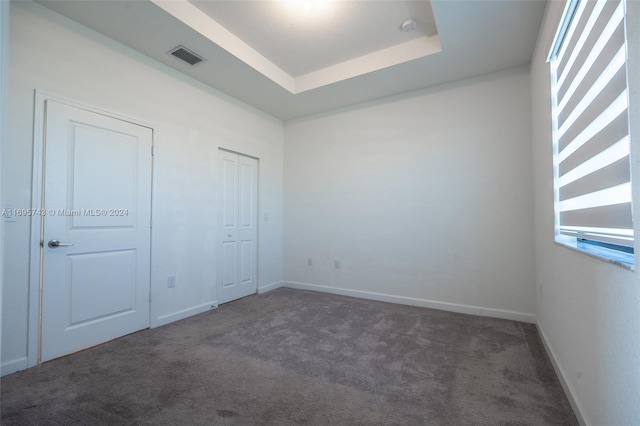 unfurnished bedroom with dark colored carpet and a raised ceiling