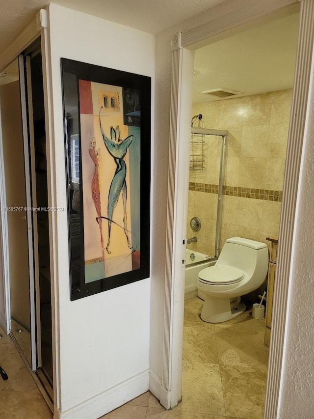 bathroom featuring tile patterned floors, toilet, and bath / shower combo with glass door