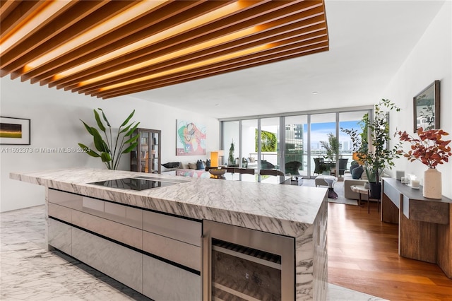 kitchen with floor to ceiling windows, wine cooler, light hardwood / wood-style floors, black electric stovetop, and a kitchen island