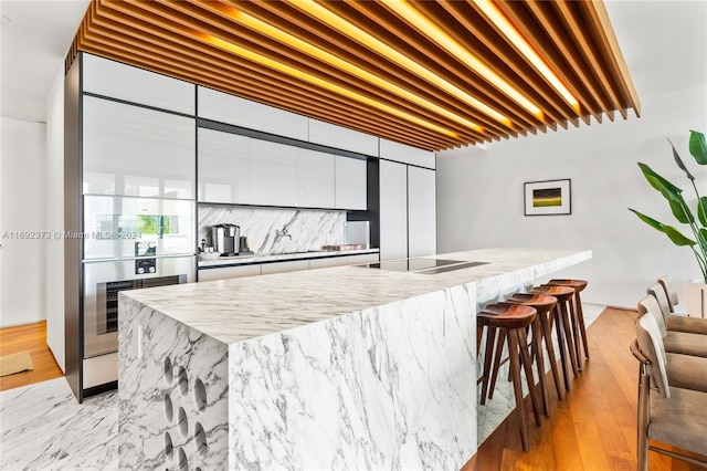 bar featuring sink, light hardwood / wood-style flooring, oven, black electric stovetop, and white cabinets