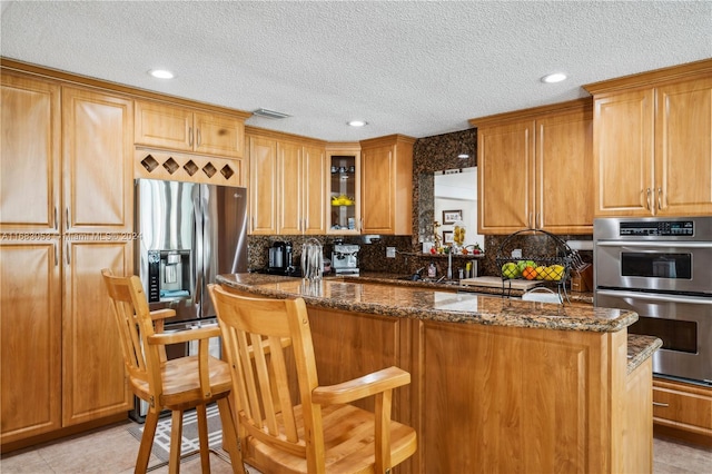 kitchen with dark stone countertops, a textured ceiling, appliances with stainless steel finishes, tasteful backsplash, and a breakfast bar area