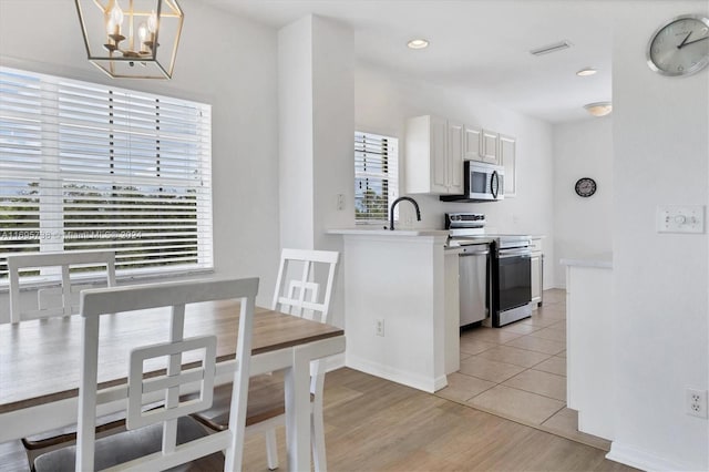 kitchen with appliances with stainless steel finishes, decorative light fixtures, white cabinetry, and plenty of natural light