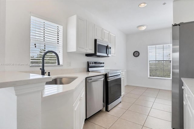 kitchen with white cabinetry, sink, stainless steel appliances, a barn door, and light tile patterned flooring