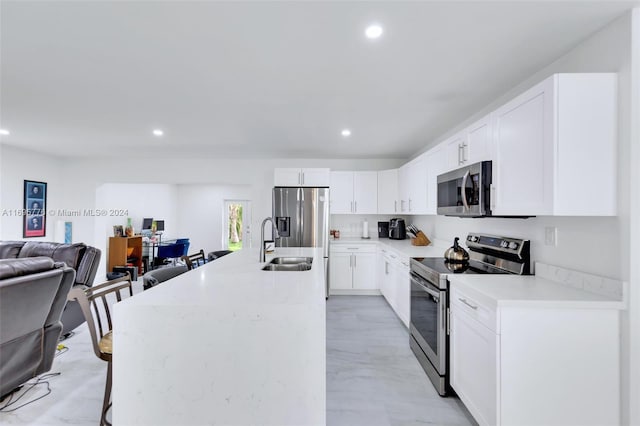 kitchen with a breakfast bar, a center island with sink, sink, white cabinetry, and stainless steel appliances