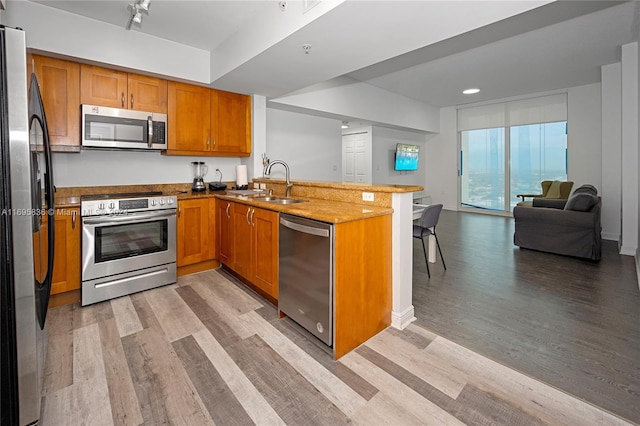 kitchen featuring kitchen peninsula, light wood-type flooring, stainless steel appliances, and light stone counters