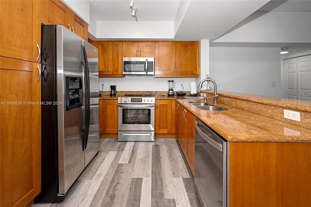 kitchen with sink, stainless steel appliances, light stone counters, kitchen peninsula, and light hardwood / wood-style floors