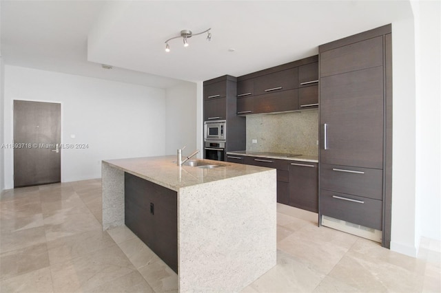 kitchen with backsplash, a kitchen island with sink, sink, dark brown cabinetry, and stainless steel appliances