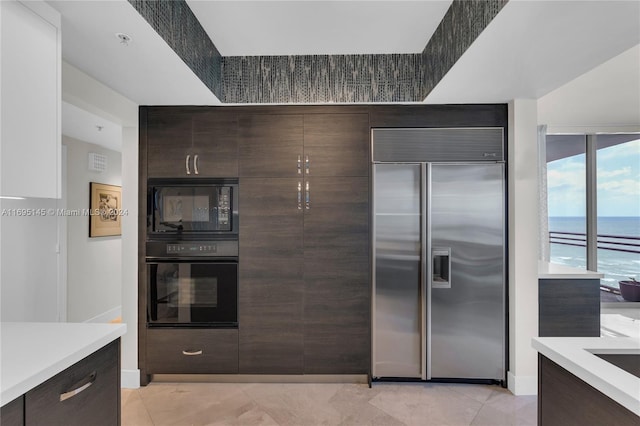 kitchen featuring light tile patterned flooring, dark brown cabinets, a water view, and black appliances